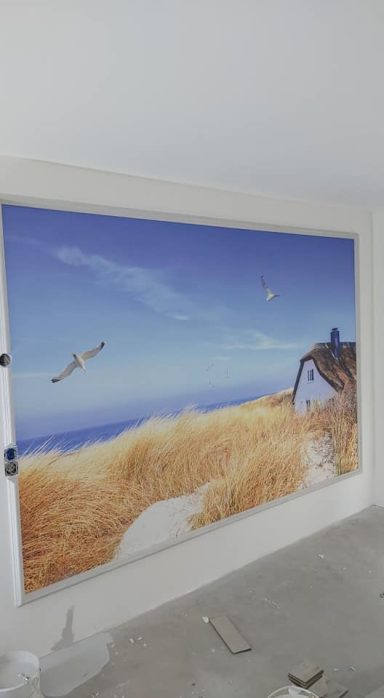 Wandmalerei mit Küstenlandschaft, Gras, Himmel und Vögeln über dem Meer.